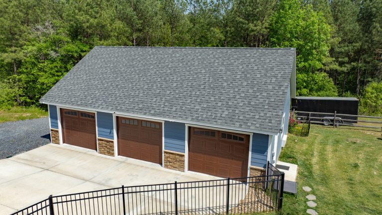 Aerial close up view of early american blue T111 smart sided 28x40 single story workshop 3-car garage with Charcoal gray Architectural Shingles, white trim, and walnut garage doors