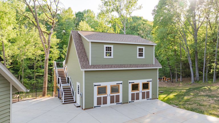Aerial view of a custom painted green with white trim garage with attic, and duel brown shingled roof