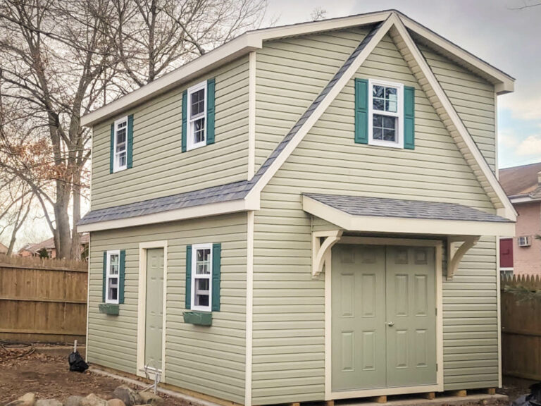 the exterior of a sage 2-story workshop shed in Farmingdale, NY with forest green shutters, charcoal gray shingles, and antique ivory trim
