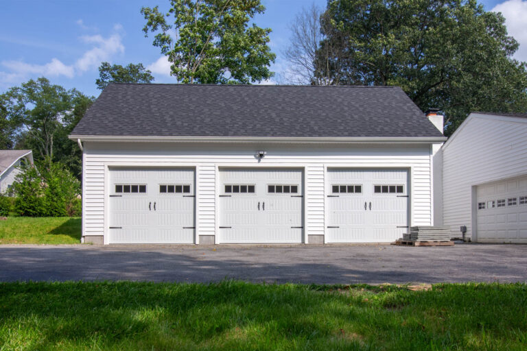 a white Attic Workshop 3-Car Garage with vinyl siding and black shutters in Carmel Hamlet, NY built by Sheds Unlimited