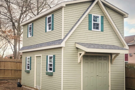 the exterior of a sage 2-story workshop shed in Farmingdale, NY with forest green shutters, charcoal gray shingles, and antique ivory trim