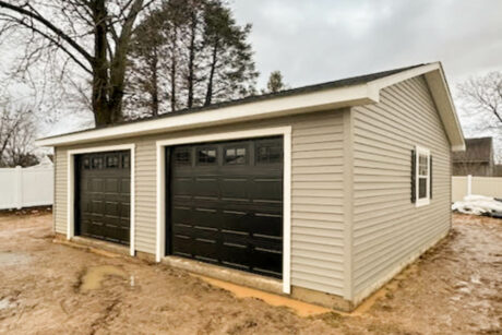 the exterior of a tan single-story workshop 2-car garage in Warminster, PA with white trim and black garage door and black shutters and a dual black roof