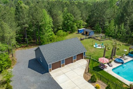 Aerial front right corner view of a early american blue T111 smart sided 28x40 single story workshop 3-car garage with Charcoal gray Architectural Shingles and white trim