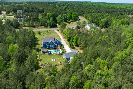 Far off Aerial rear view of a early american blue T111 smart sided 28x40 single story workshop 3-car garage with Charcoal gray Architectural Shingles and white trim
