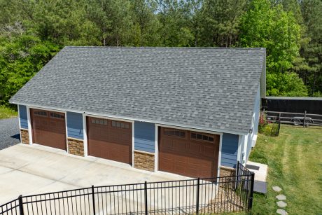 Aerial close up view of early american blue T111 smart sided 28x40 single story workshop 3-car garage with Charcoal gray Architectural Shingles, white trim, and walnut garage doors