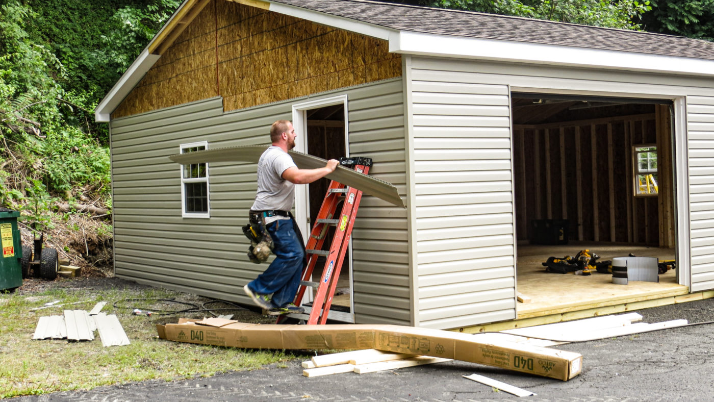 exterior of double wide shed with worker putting on siding